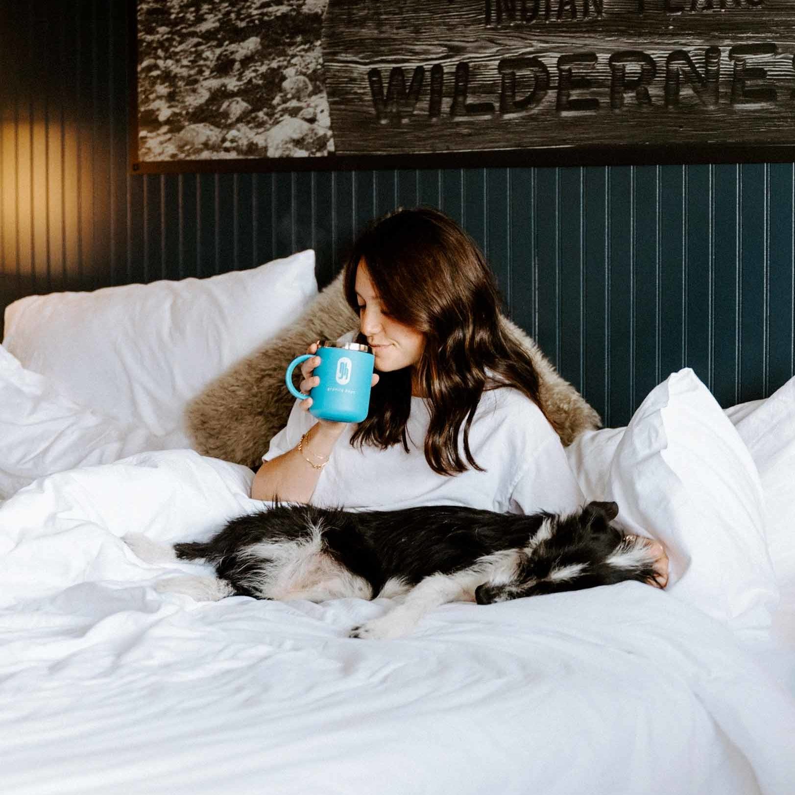 Gravity Haus Winter Park guest enjoying beverage in bed with pup