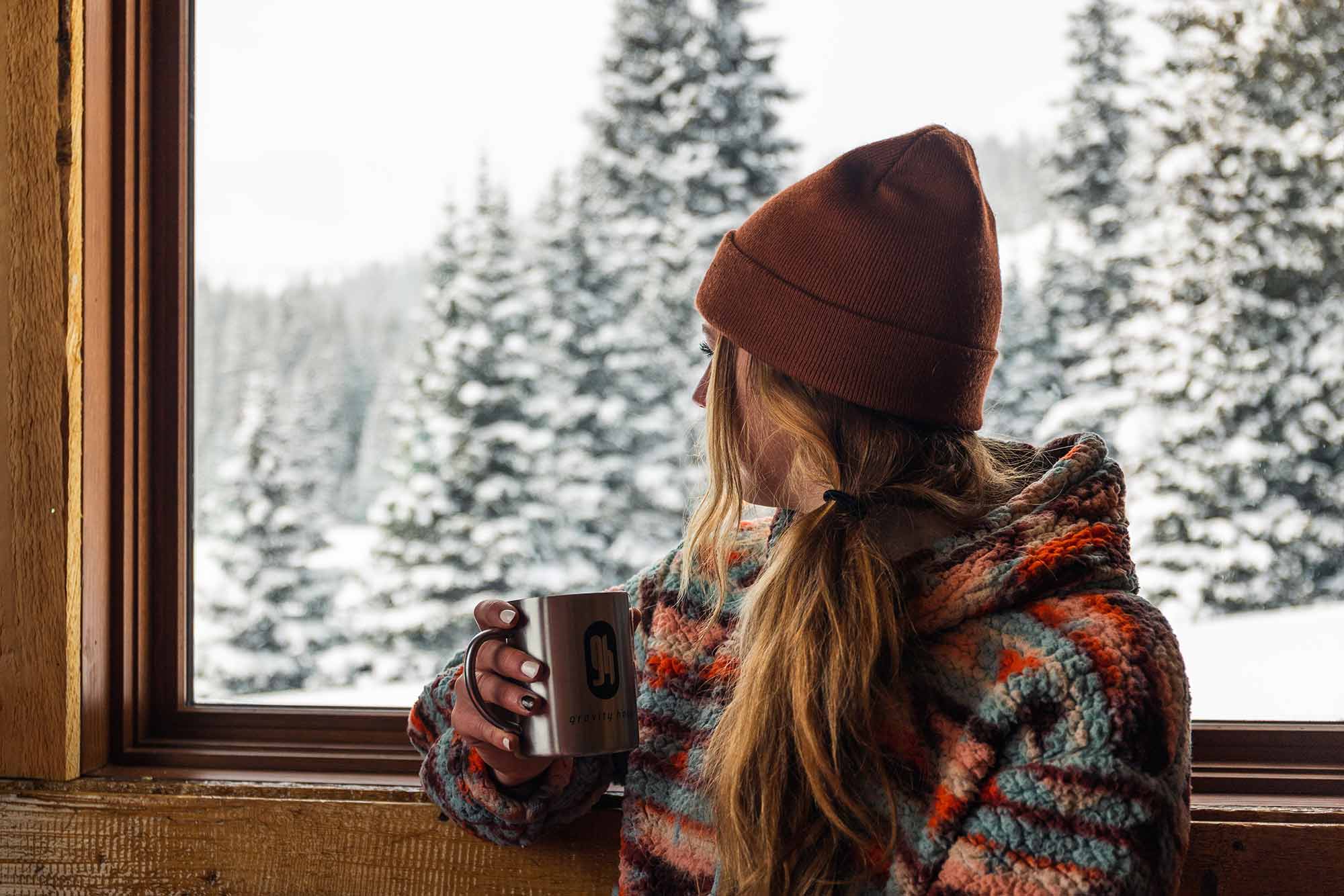 Woman with GH branded mug and beanie enjoying winter view from cabin.
