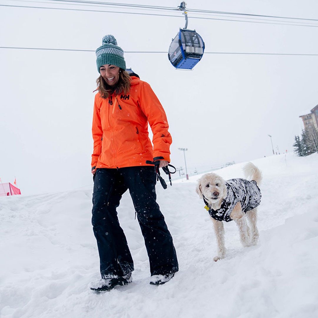 Valerie Seid and pup walking outside Gravity Haus Steamboat on a snowy day with gondola in background.
