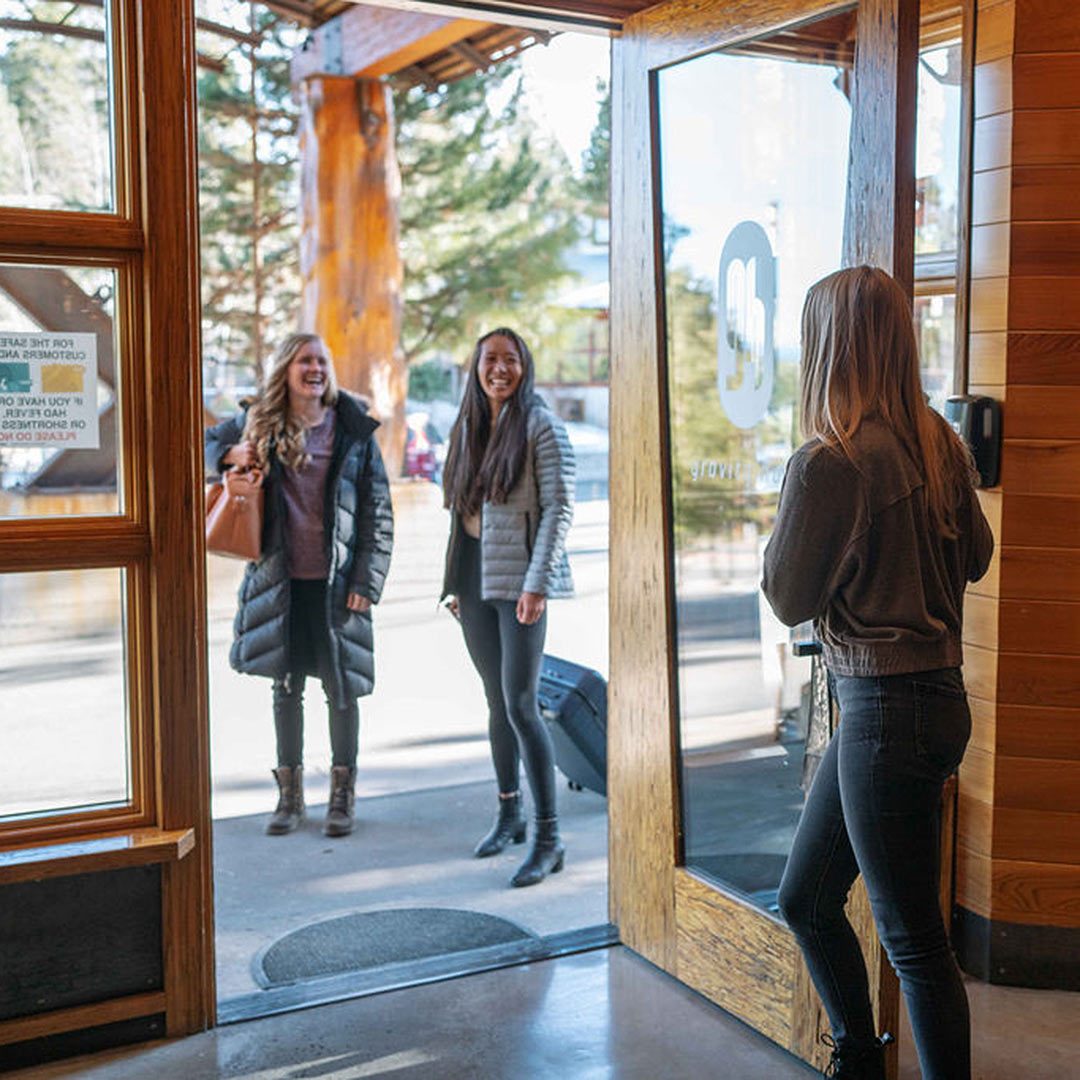 Two women arrive at the Gravity Haus Truckee Tahoe entrance, welcomed by a third.