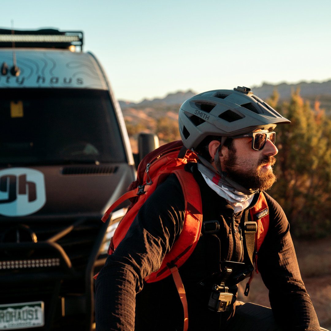 Mountain biker preparing to set out with Gravity Haus branded van in background in Moab, UT.