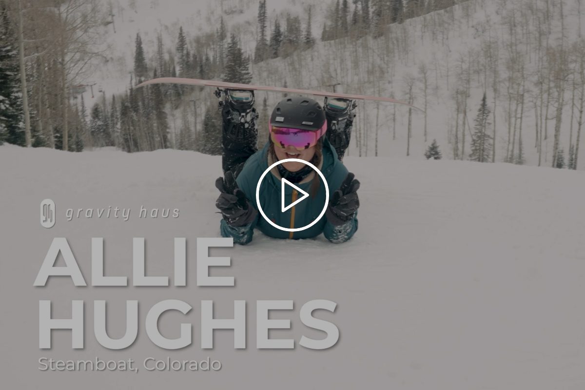 Allie Hughes belly sliding on her snowboard on a snowy day outside Gravity Haus Steamboat