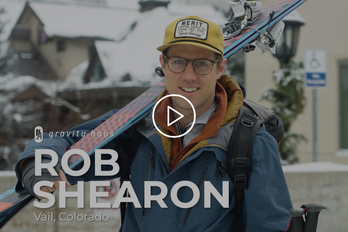 Rob Shearon with yellow Gravity Haus cap carrying skis