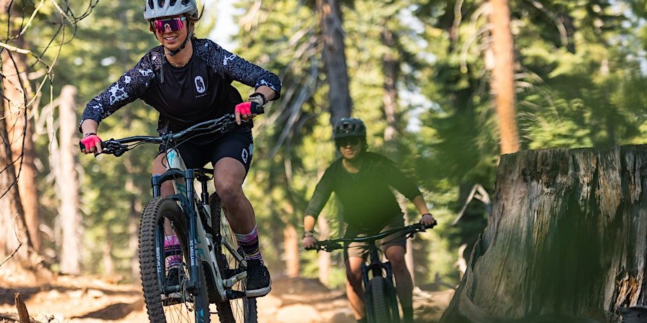 Two women smiling mountain biking in summer forest